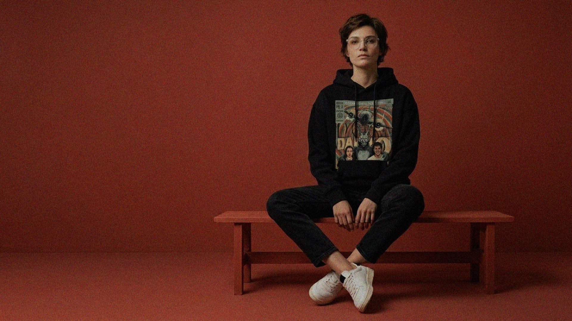 Model sitting on bench wearing Sukiprime retro vintage comic cover hoodie inspired by Donnie Darko featuring classic comic book style artwork.